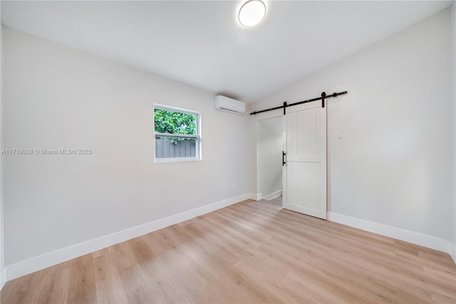 spare room featuring vaulted ceiling, a barn door, an AC wall unit, and light hardwood / wood-style floors