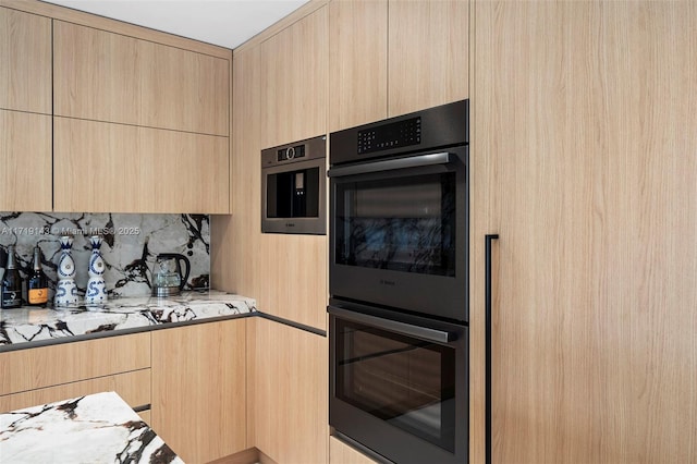 kitchen featuring light stone countertops, light brown cabinetry, and multiple ovens