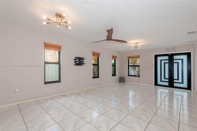 empty room featuring ceiling fan with notable chandelier, french doors, a healthy amount of sunlight, and light tile patterned flooring