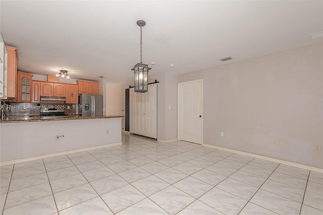 kitchen with decorative light fixtures, dark stone countertops, backsplash, stainless steel appliances, and a barn door