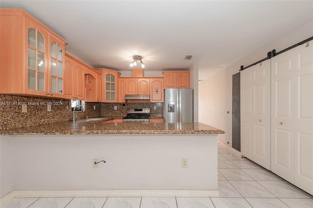 kitchen with sink, appliances with stainless steel finishes, kitchen peninsula, stone counters, and a barn door