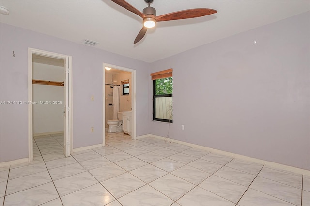 unfurnished bedroom featuring ceiling fan, connected bathroom, light tile patterned flooring, a spacious closet, and a closet