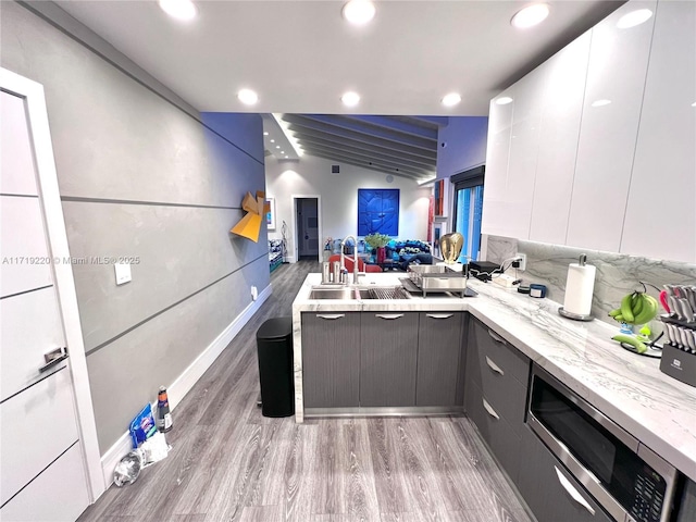 kitchen with light stone countertops, stainless steel microwave, sink, wood-type flooring, and white cabinets