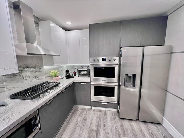 kitchen with decorative backsplash, wall chimney exhaust hood, light hardwood / wood-style floors, stainless steel appliances, and gray cabinets