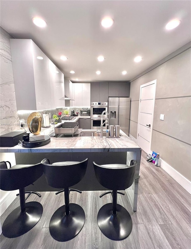 kitchen featuring gray cabinetry, a breakfast bar, light wood-type flooring, appliances with stainless steel finishes, and kitchen peninsula