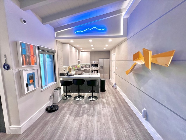 interior space featuring appliances with stainless steel finishes, light wood-type flooring, lofted ceiling with beams, white cabinetry, and a breakfast bar area