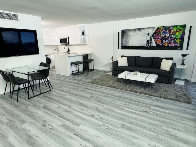 living room featuring washer / clothes dryer, sink, and light hardwood / wood-style flooring