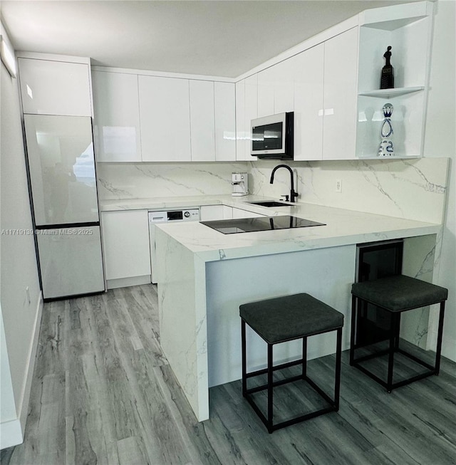 kitchen featuring kitchen peninsula, backsplash, a breakfast bar, sink, and white cabinets