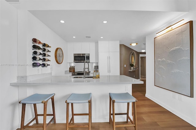 kitchen with a breakfast bar, dark hardwood / wood-style floors, white cabinetry, kitchen peninsula, and stainless steel appliances