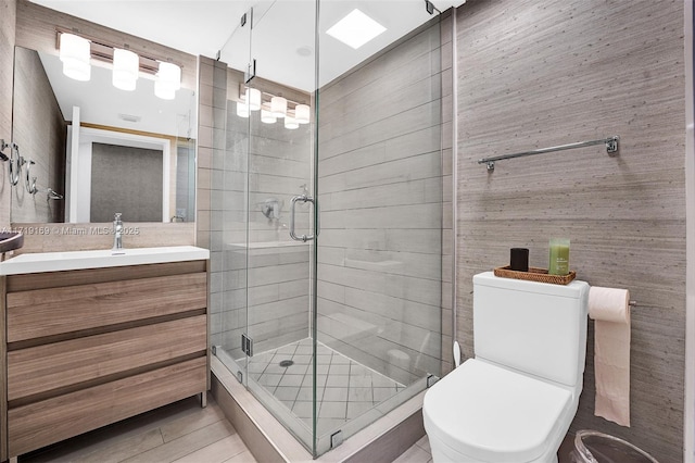 bathroom with a skylight, vanity, a shower with shower door, and toilet