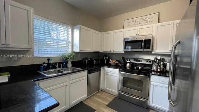 kitchen featuring sink, white cabinets, light hardwood / wood-style floors, stainless steel appliances, and a textured ceiling