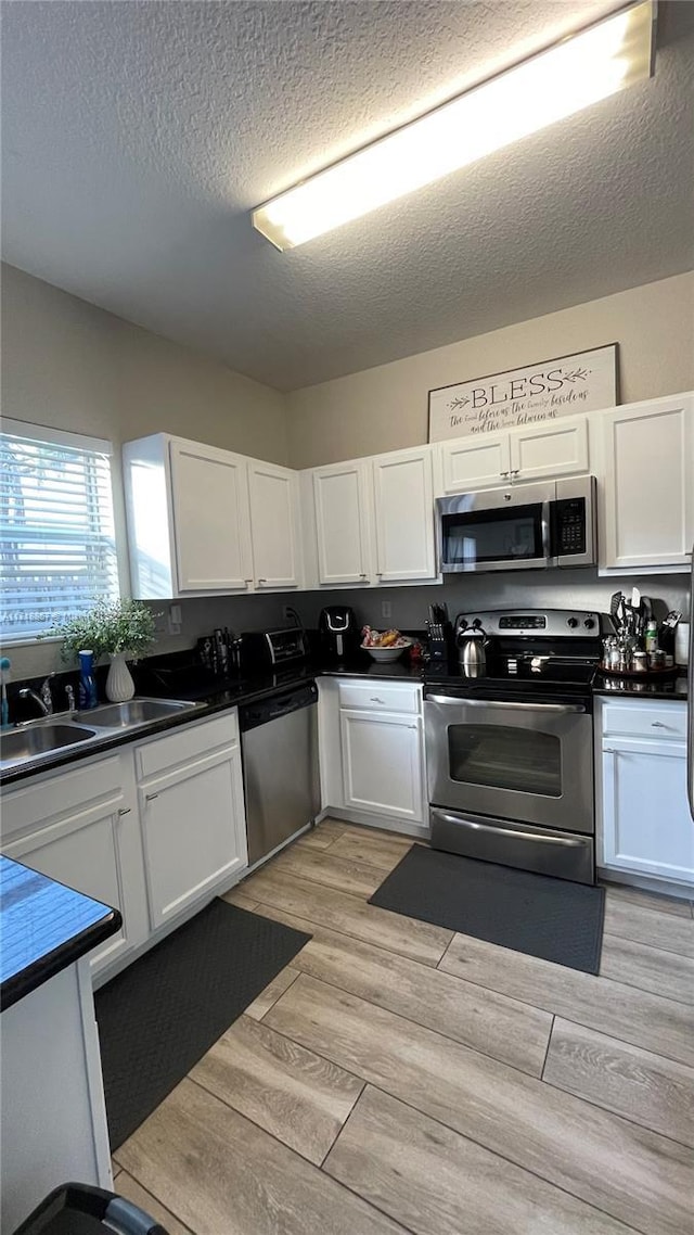 kitchen featuring stainless steel appliances, white cabinetry, a textured ceiling, and light wood-type flooring