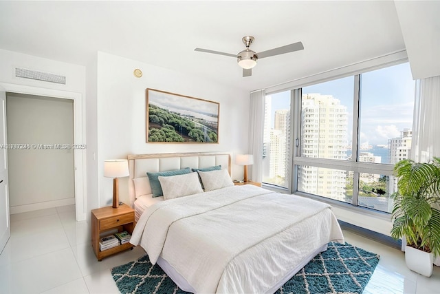 tiled bedroom featuring multiple windows, ceiling fan, and a wall of windows