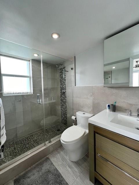 bathroom with vanity, toilet, walk in shower, and tile walls