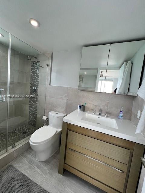 bathroom with tasteful backsplash, an enclosed shower, toilet, vanity, and tile walls