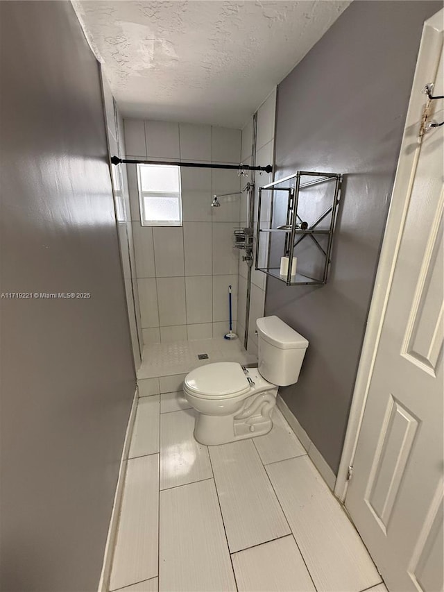 bathroom with toilet, a textured ceiling, and a tile shower