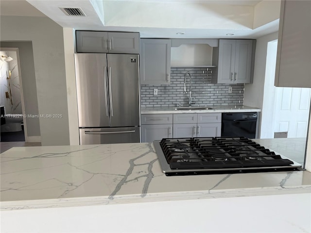 kitchen with light stone counters, black appliances, decorative backsplash, gray cabinets, and sink