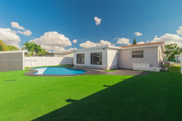 rear view of house featuring a fenced in pool, stucco siding, fence, and a lawn