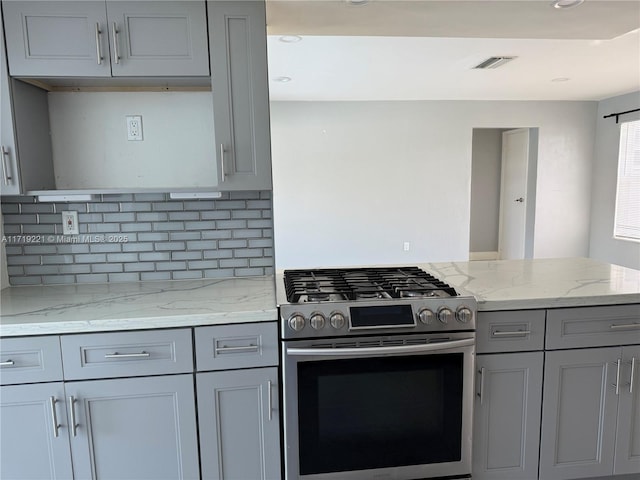 kitchen featuring light stone counters, tasteful backsplash, kitchen peninsula, stainless steel gas range oven, and gray cabinets