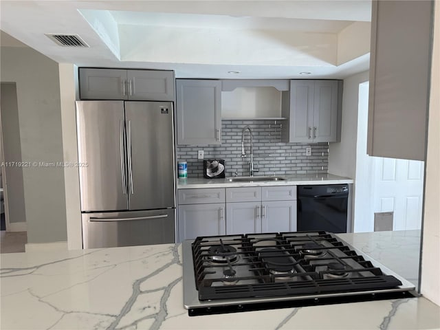 kitchen with stovetop, stainless steel fridge, sink, black dishwasher, and tasteful backsplash