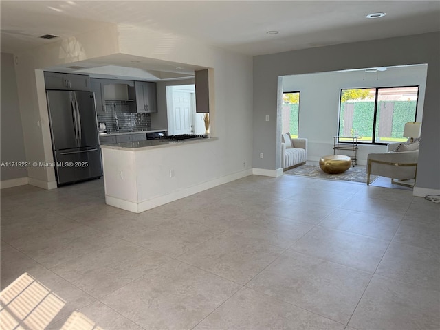 kitchen featuring light tile patterned flooring, tasteful backsplash, kitchen peninsula, and stainless steel fridge