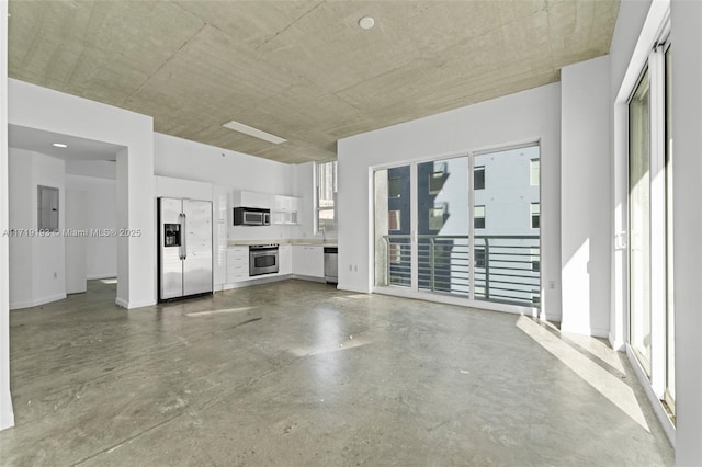 unfurnished living room with concrete flooring, electric panel, and a healthy amount of sunlight