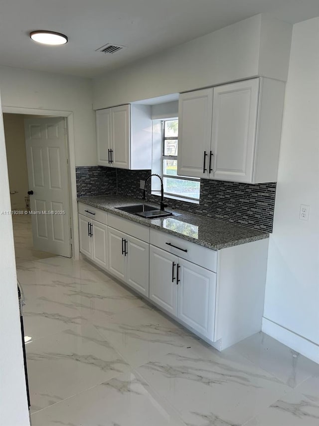 kitchen with backsplash, white cabinetry, sink, and dark stone counters