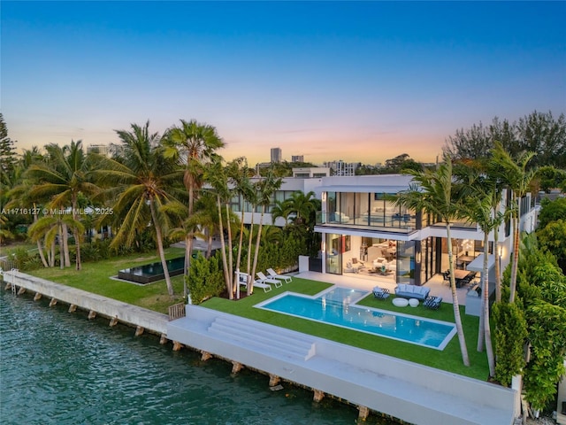 315 N Shore Dr, Miami Beach, FL 33141 - back of house at dusk with a water view, an outdoor pool, a yard, and a balcony