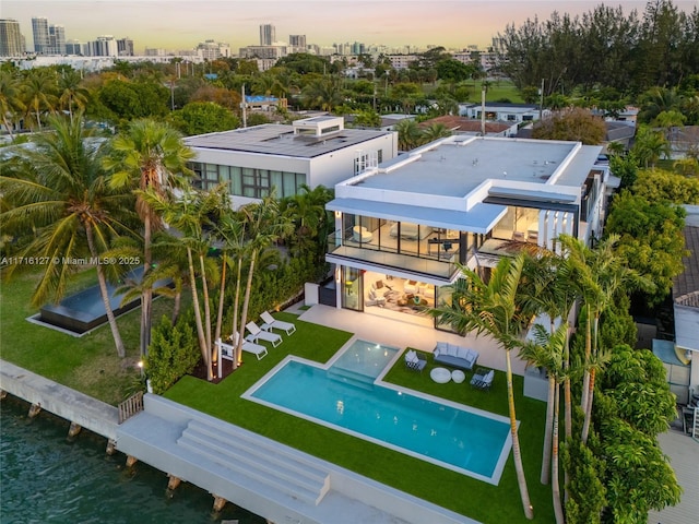 315 N Shore Dr, Miami Beach, FL 33141 - back of house at dusk with a patio, a view of city, an outdoor pool, a fenced backyard, and a lawn