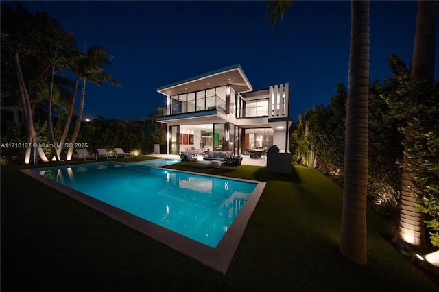 315 N Shore Dr, Miami Beach, FL 33141 - back of house at night featuring a balcony, outdoor lounge area, an outdoor pool, a patio area, and a yard