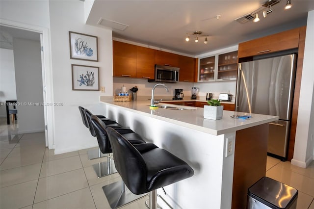 kitchen featuring sink, a kitchen breakfast bar, kitchen peninsula, light tile patterned floors, and appliances with stainless steel finishes