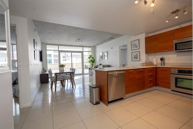 kitchen with floor to ceiling windows, sink, light tile patterned floors, appliances with stainless steel finishes, and kitchen peninsula