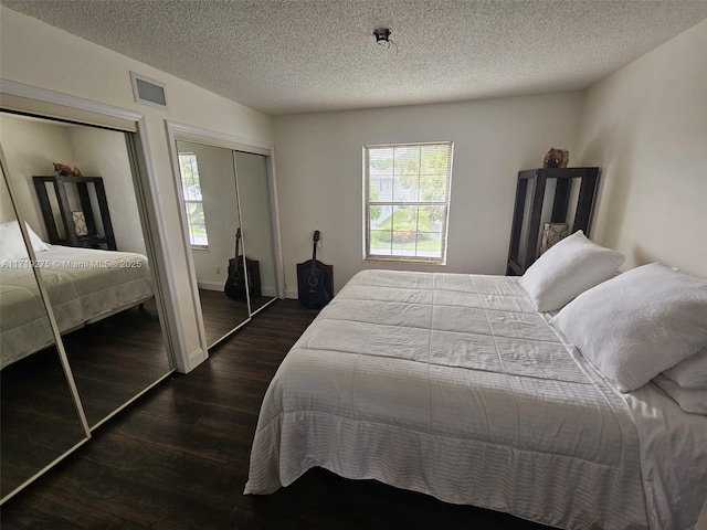 bedroom with dark hardwood / wood-style floors, a textured ceiling, and multiple closets