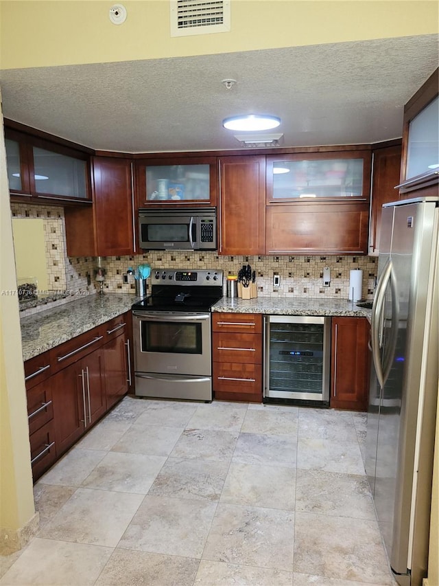 kitchen with light stone countertops, decorative backsplash, a textured ceiling, stainless steel appliances, and wine cooler