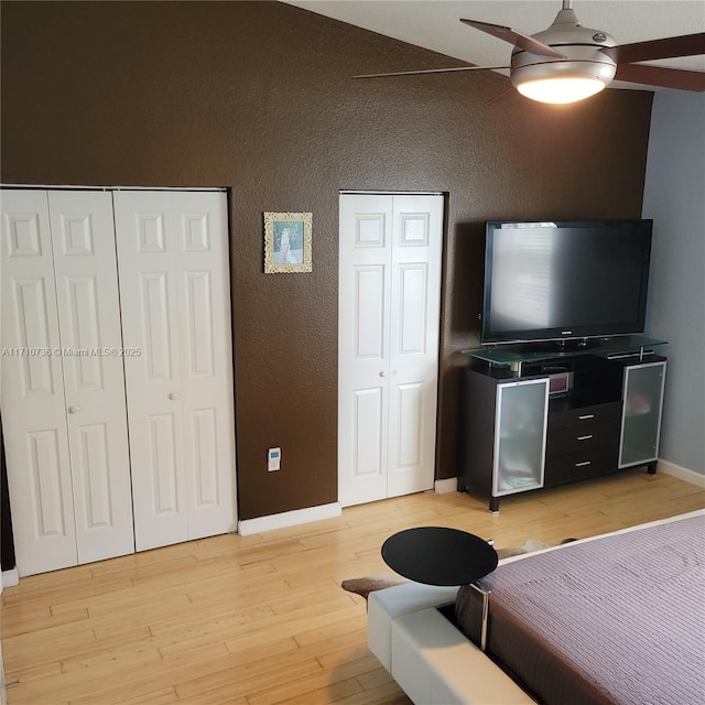 bedroom with two closets, ceiling fan, light hardwood / wood-style flooring, and vaulted ceiling