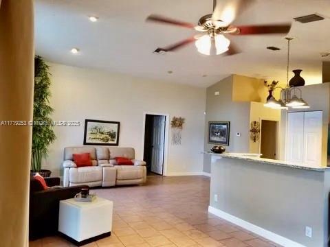 tiled living room featuring ceiling fan with notable chandelier