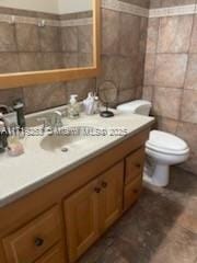 bathroom with vanity, toilet, and tile walls