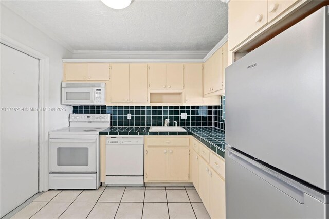 kitchen featuring tasteful backsplash, sink, light tile patterned floors, stainless steel refrigerator, and tile counters