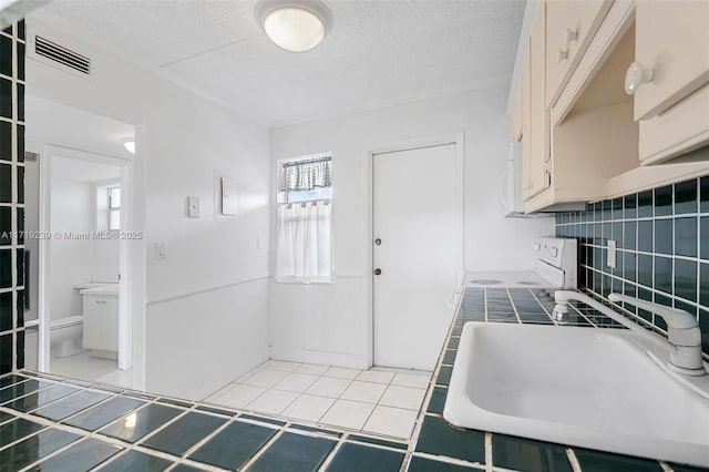 kitchen featuring sink, tile patterned flooring, backsplash, tile counters, and a textured ceiling