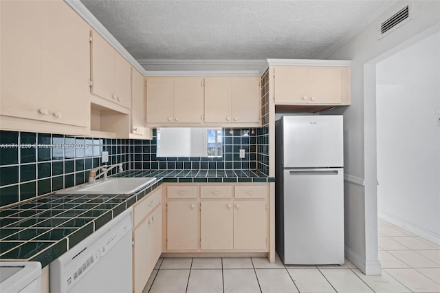 kitchen featuring cream cabinets, white dishwasher, refrigerator, and sink