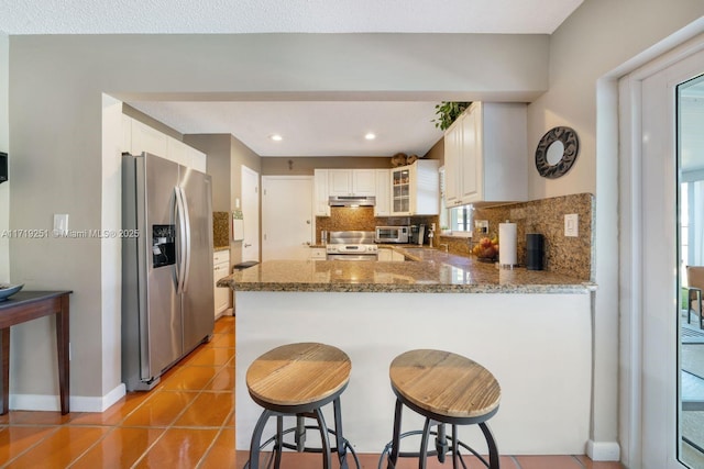 kitchen featuring kitchen peninsula, backsplash, stainless steel appliances, light tile patterned floors, and a breakfast bar area