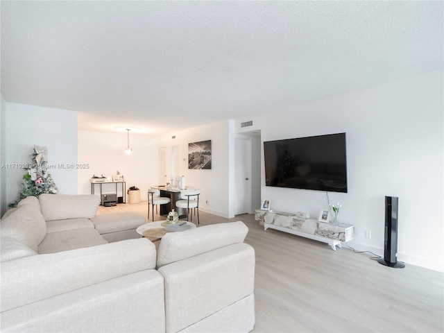 living area featuring light wood-style floors, a textured ceiling, and visible vents