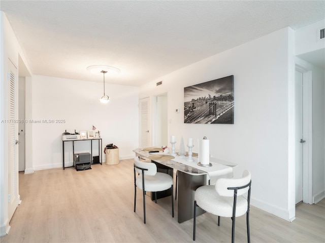 dining room featuring light wood-style flooring, a textured ceiling, baseboards, and visible vents