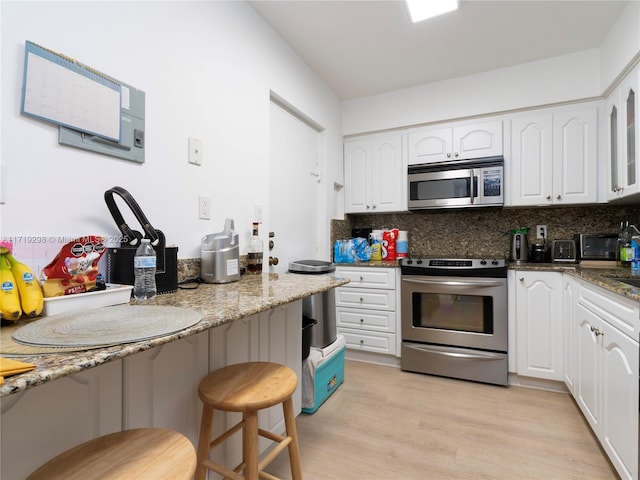 kitchen featuring a breakfast bar, white cabinetry, light wood-style floors, decorative backsplash, and appliances with stainless steel finishes