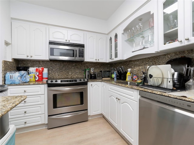kitchen featuring stone countertops, glass insert cabinets, white cabinetry, backsplash, and stainless steel appliances