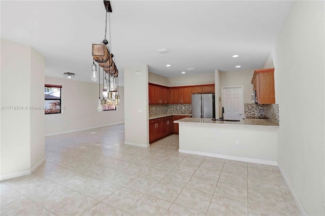 kitchen with kitchen peninsula, stainless steel fridge, backsplash, light tile patterned floors, and hanging light fixtures