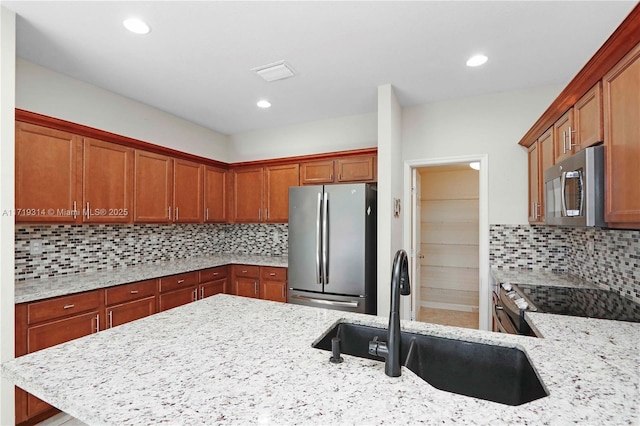 kitchen with tasteful backsplash, light stone counters, sink, and appliances with stainless steel finishes