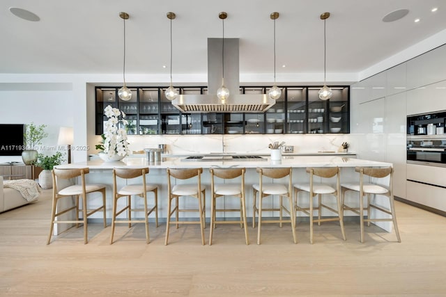 kitchen with a kitchen breakfast bar, light wood-type flooring, decorative light fixtures, and island range hood