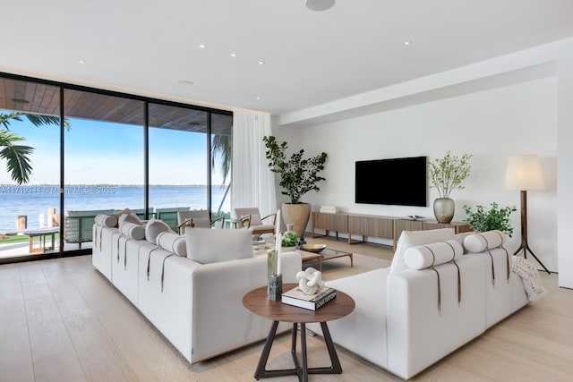 living room with expansive windows, a water view, and light hardwood / wood-style floors