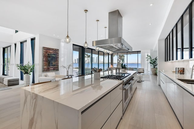 kitchen with a water view, range with two ovens, decorative light fixtures, a large island, and island range hood